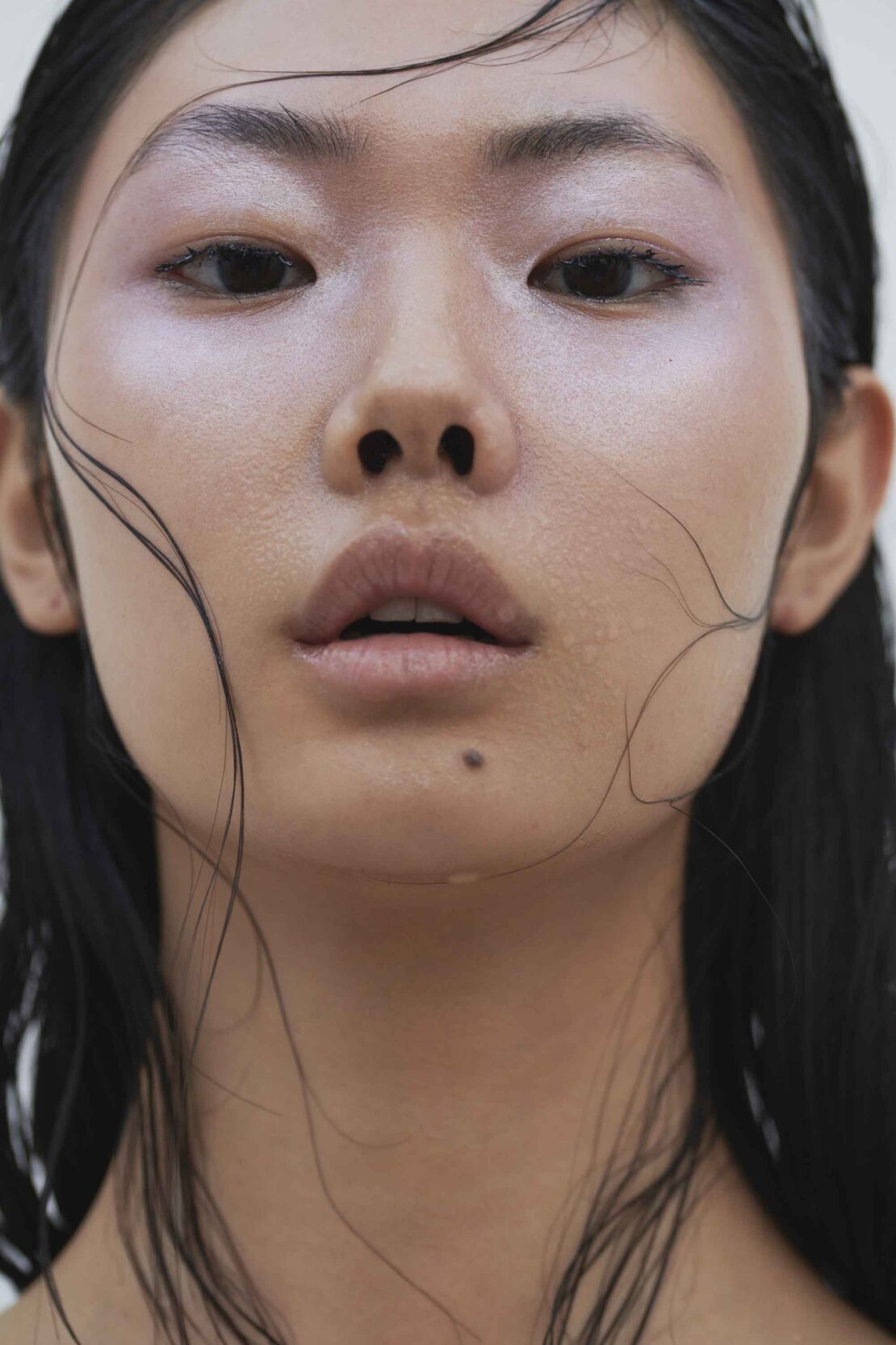 Close-up portrait of an Asian adult female with dark hair, shiny skin, and neutral expression against a white background.