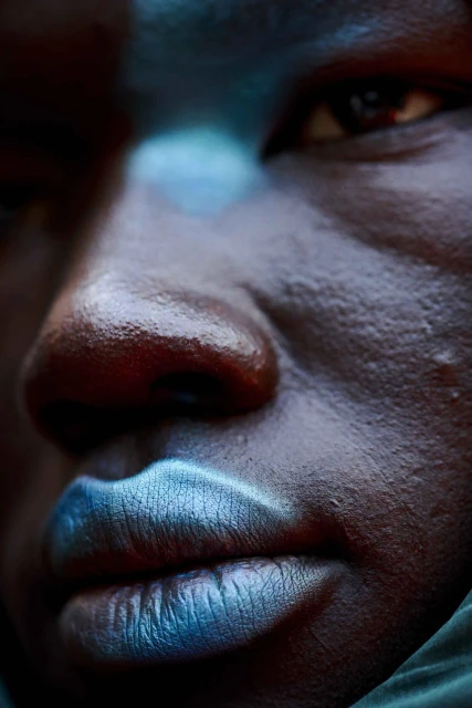 Dramatic close-up of an adult with dark skin featuring bright blue lipstick and partial facial highlights, enhancing facial details.