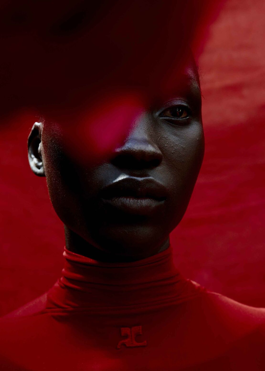 Close-up portrait of an African American woman with dark skin in red top, set against a monochrome dark-red background, dramatic lighting.