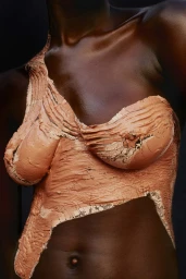 Close-up portrait of a Black woman wearing textured peach-colored clay sculpted over her torso and shoulder by photographer Ekua King.