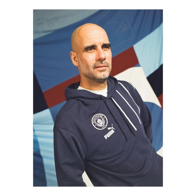 Portrait of a man in a dark blue Manchester City hoodie with a backdrop of light blue, red, and dark blue fabric.