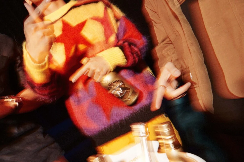 Close-up of two people at a party, one wearing a multicolored star sweater and holding a champagne bottle in a blurry, energetic photo.