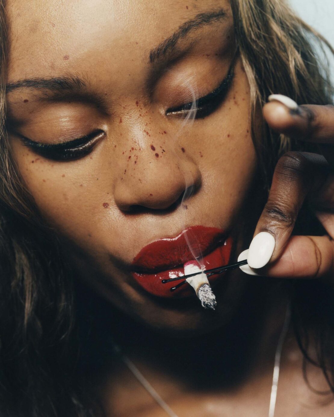 Close-up portrait of a woman with red lipstick holding a lit cigarette between her lips, emphasizing beauty and a smoky atmosphere.
