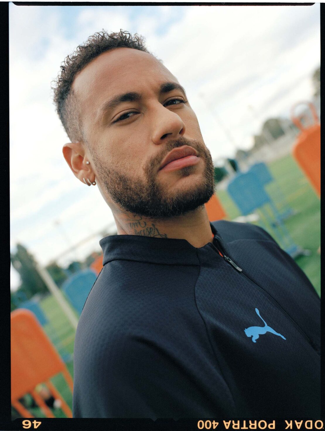 Portrait of a light-skinned adult male wearing a black Puma jacket, looking at the camera with a blurred outdoor background.