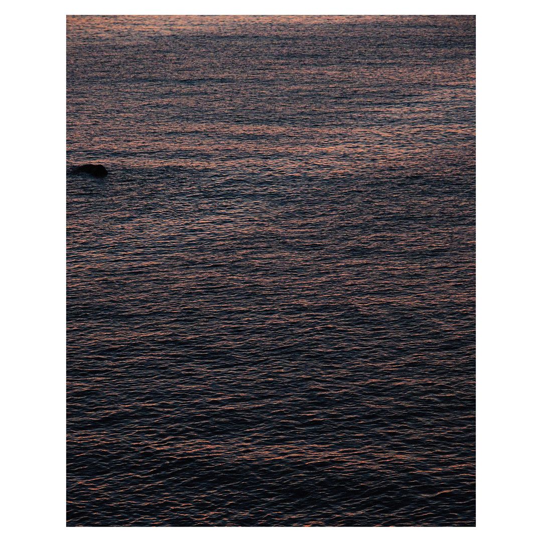 Dark rippling ocean water at twilight with a single small rock visible near the left edge