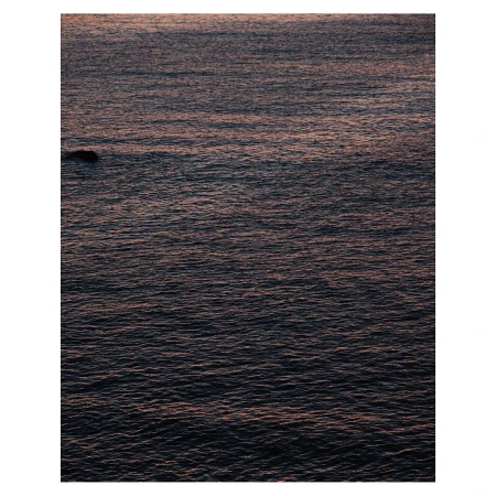 Dark rippling ocean water at twilight with a single small rock visible near the left edge