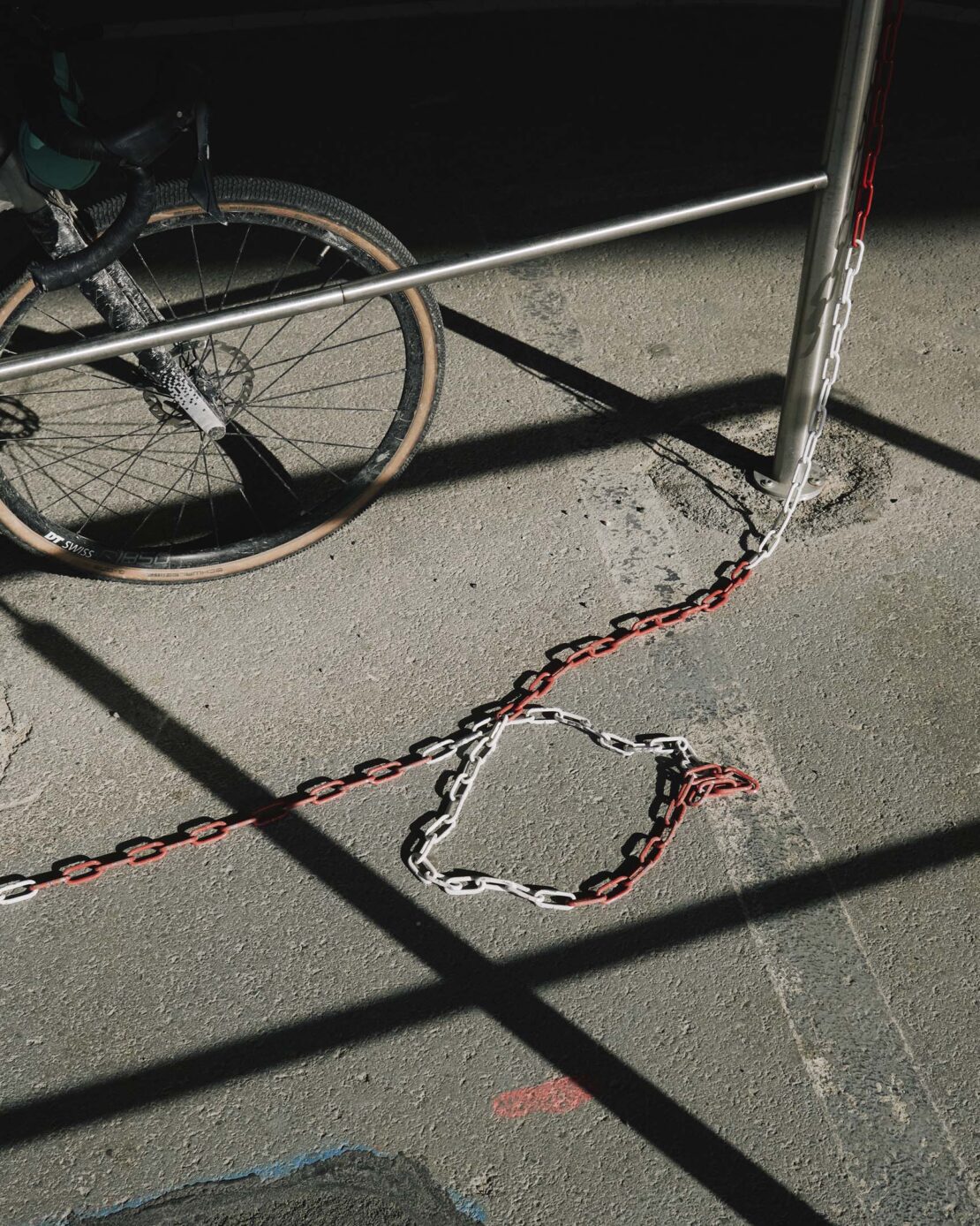 An eye-level shot on an urban sidewalk featuring a gravel bicycle leaning against a metal railing, accented by a red and white chain.