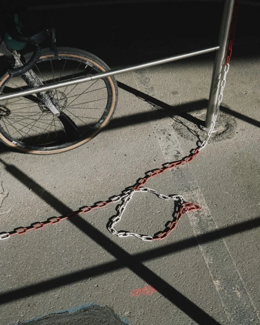 An eye-level shot on an urban sidewalk featuring a gravel bicycle leaning against a metal railing, accented by a red and white chain.