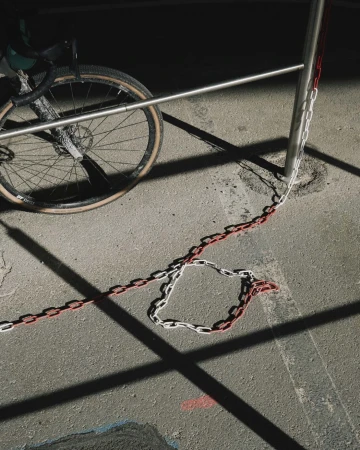 An eye-level shot on an urban sidewalk featuring a gravel bicycle leaning against a metal railing, accented by a red and white chain.
