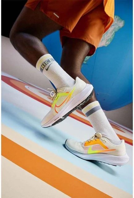 Running shoes by Nike on a light blue and orange surface, modelled by an African-American adult wearing orange shorts and socks.