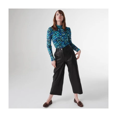 Model wearing a blue floral turtleneck and black leather cropped trousers against a white seamless studio backdrop.