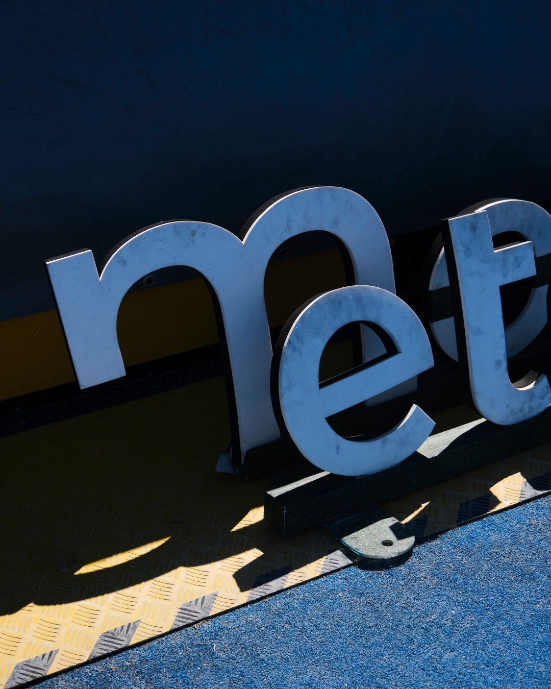 Elevated shot of large free-standing, silver block letters spelling 'met' on top of yellow and blue platform, with strong lighting.