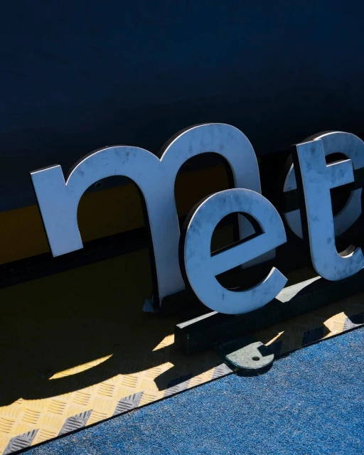 Elevated shot of large free-standing, silver block letters spelling 'met' on top of yellow and blue platform, with strong lighting.