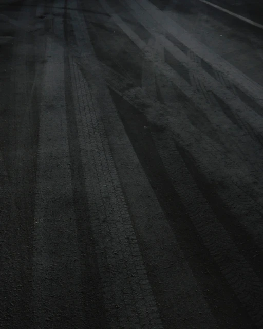 Black asphalt road surface shows clear tire tracks creating textured linear patterns, emphasizing transportation and road usage at night.