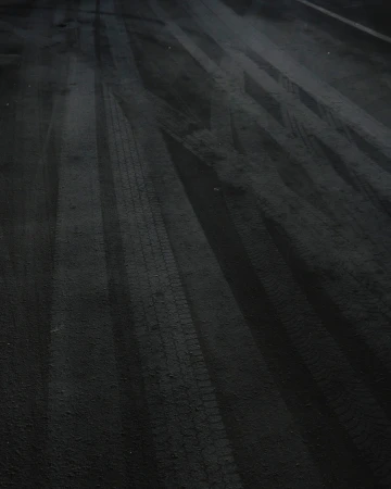 Black asphalt road surface shows clear tire tracks creating textured linear patterns, emphasizing transportation and road usage at night.