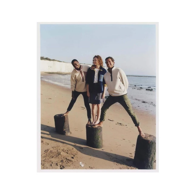 Three friends balance on concrete posts at the beach. A sunny day with sandy beach, gentle waves, and chalk cliffs in the background.