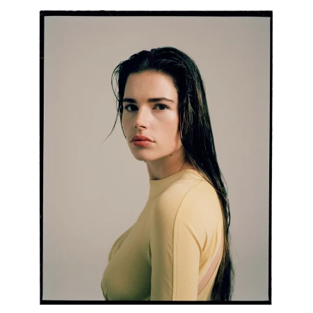 Portrait of a woman with long dark wet hair wearing a yellow top against a plain studio background.