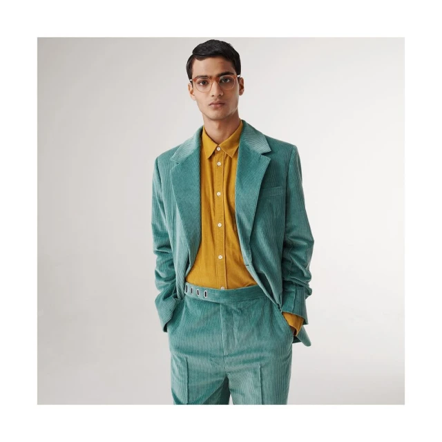 Adult male in glasses wearing a corduroy suit and shirt in a studio setting with a neutral background, posing for a fashion shot.