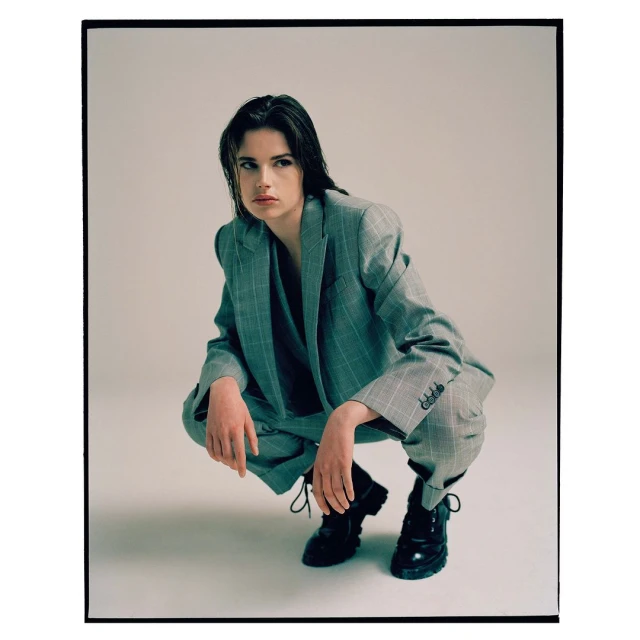 Woman in a grey plaid suit crouching in a studio, looking away with wet hair and black boots in a fashion style editorial shot.