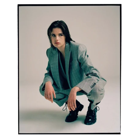 Woman in a grey plaid suit crouching in a studio, looking away with wet hair and black boots in a fashion style editorial shot.