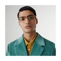 Man wearing round glasses, a yellow shirt, and a teal corduroy blazer against a plain white background