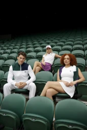 Three models seated in stadium seats wearing athletic apparel including white tennis dresses and a colour-blocked track jacket.