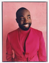 Portrait of a smiling Black man in a vibrant pink turtleneck and matching jacket against a textured pink backdrop