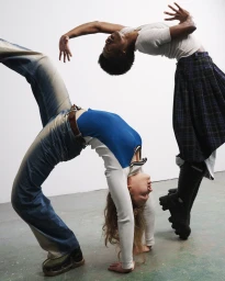 Two dancers bending backward in dynamic poses against a white studio wall and green floor