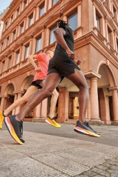Two runners in motion on a city street in front of a classical stone building, photographed by Elliott Wilcox.