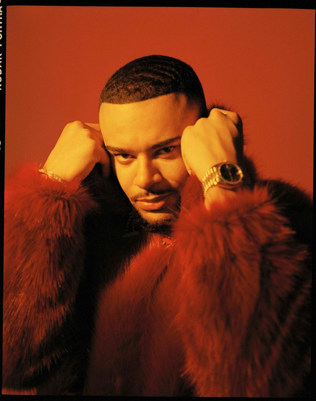 Portrait of a man in a textured red fur coat holding his collar against a matching red studio background, photographed by Elliott Wilcox.