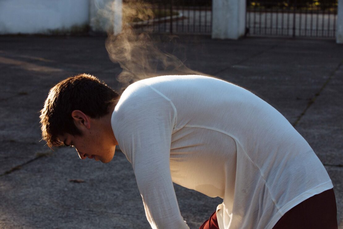 Man wearing a white long-sleeve shirt with steam rising from his back outdoors