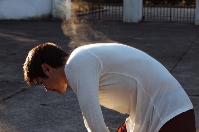 Man wearing a white long-sleeve shirt with steam rising from his back outdoors