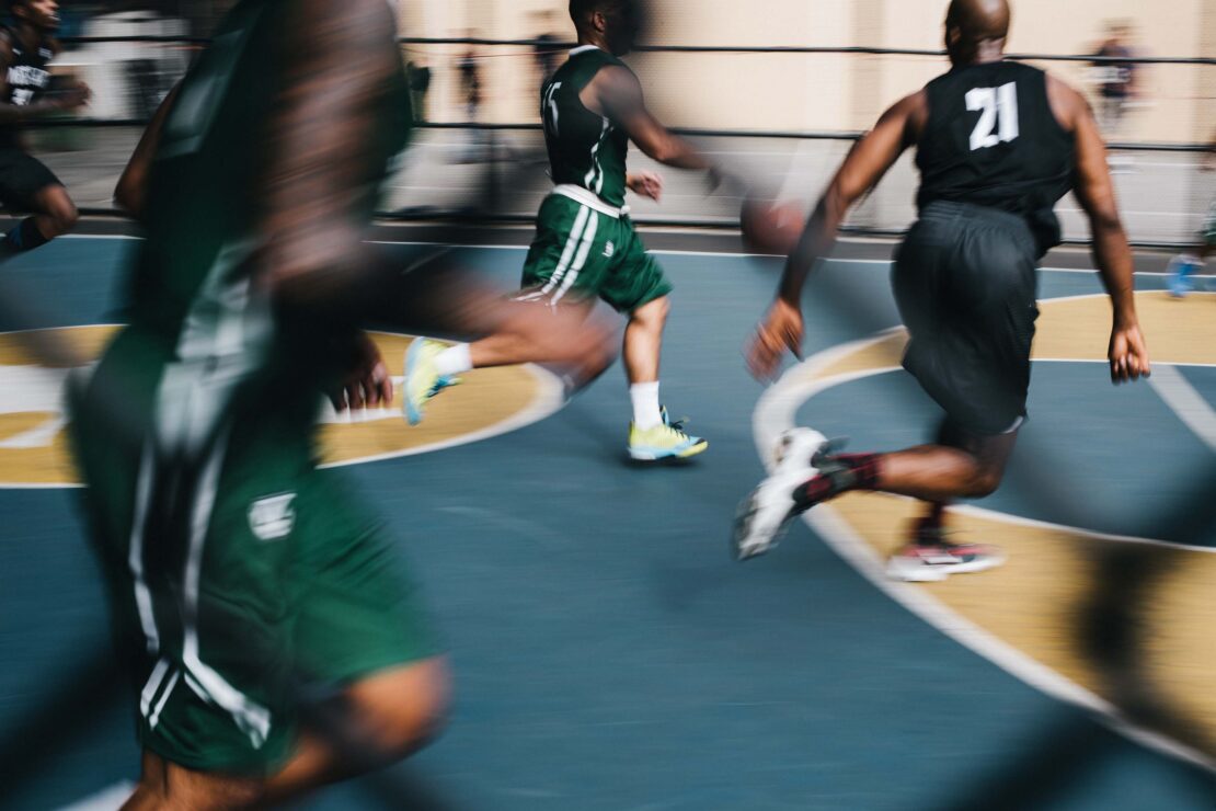 Action shot of a group of African American basketball players with basketball on an indoor court with motion blur and focus on action.