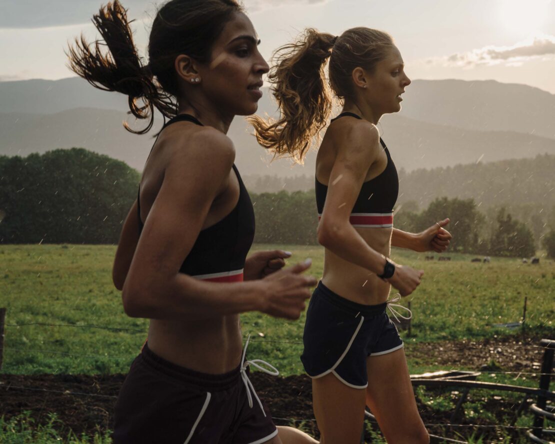 Two women jogging outdoors in sports bras and shorts, athletic and healthy lifestyle, fitness in nature, working out together.