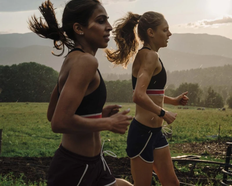 Two women jogging outdoors in sports bras and shorts, athletic and healthy lifestyle, fitness in nature, working out together.