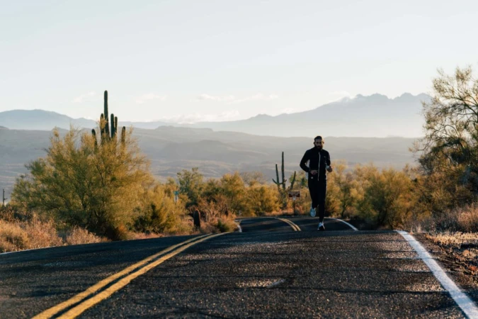 Man running on desert road at sunrise. Outdoor fitness scene with mountains, cacti, and clear sky in a lifestyle shot.