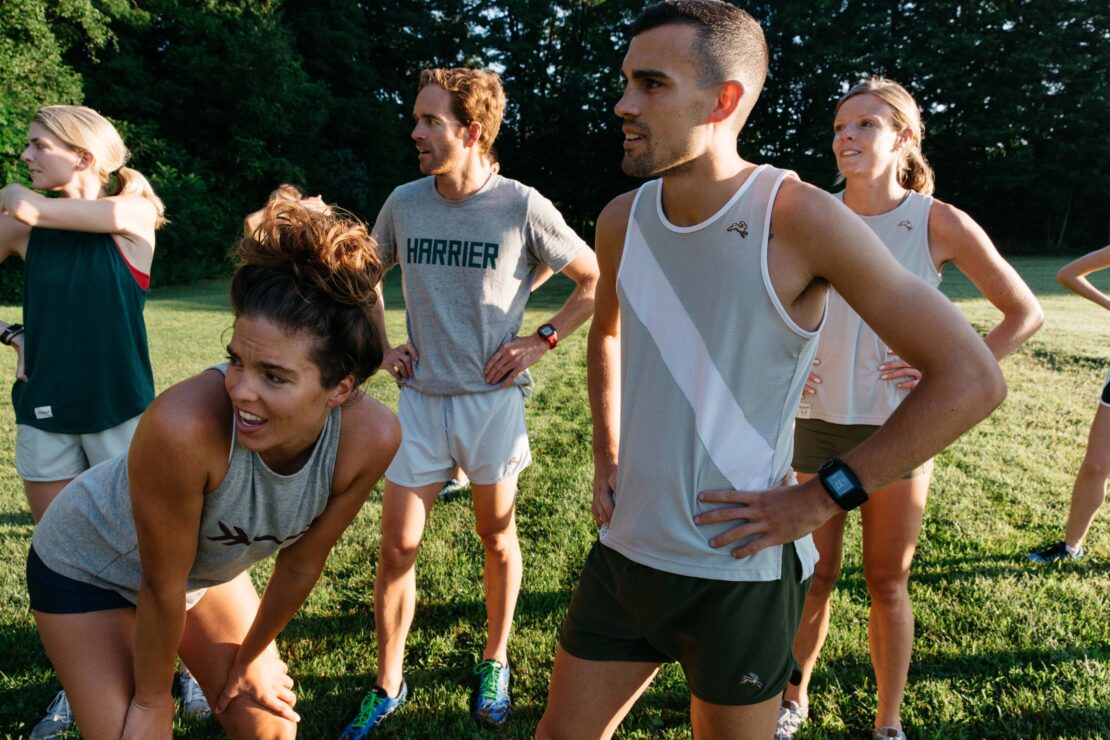 Group of runners resting on a grassy field outdoors in daylight photographed by Emily Maye.