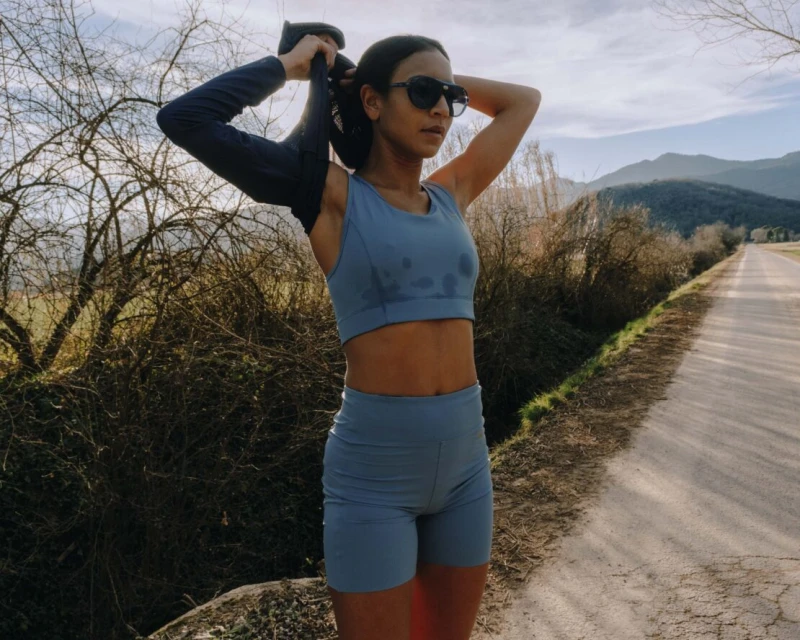 Active woman in sportswear cools down after a workout on a rural road with mountains and trees in the background on a sunny day.