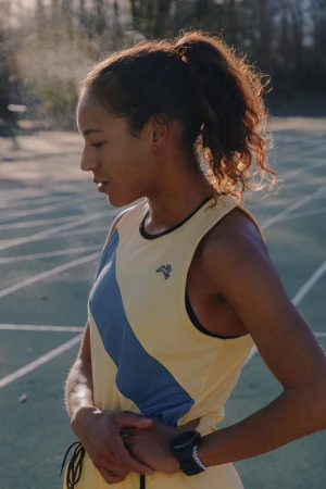 Female athlete pauses with hands on her hips on a running track. Mist rises from her body as she looks slightly down and to the left.