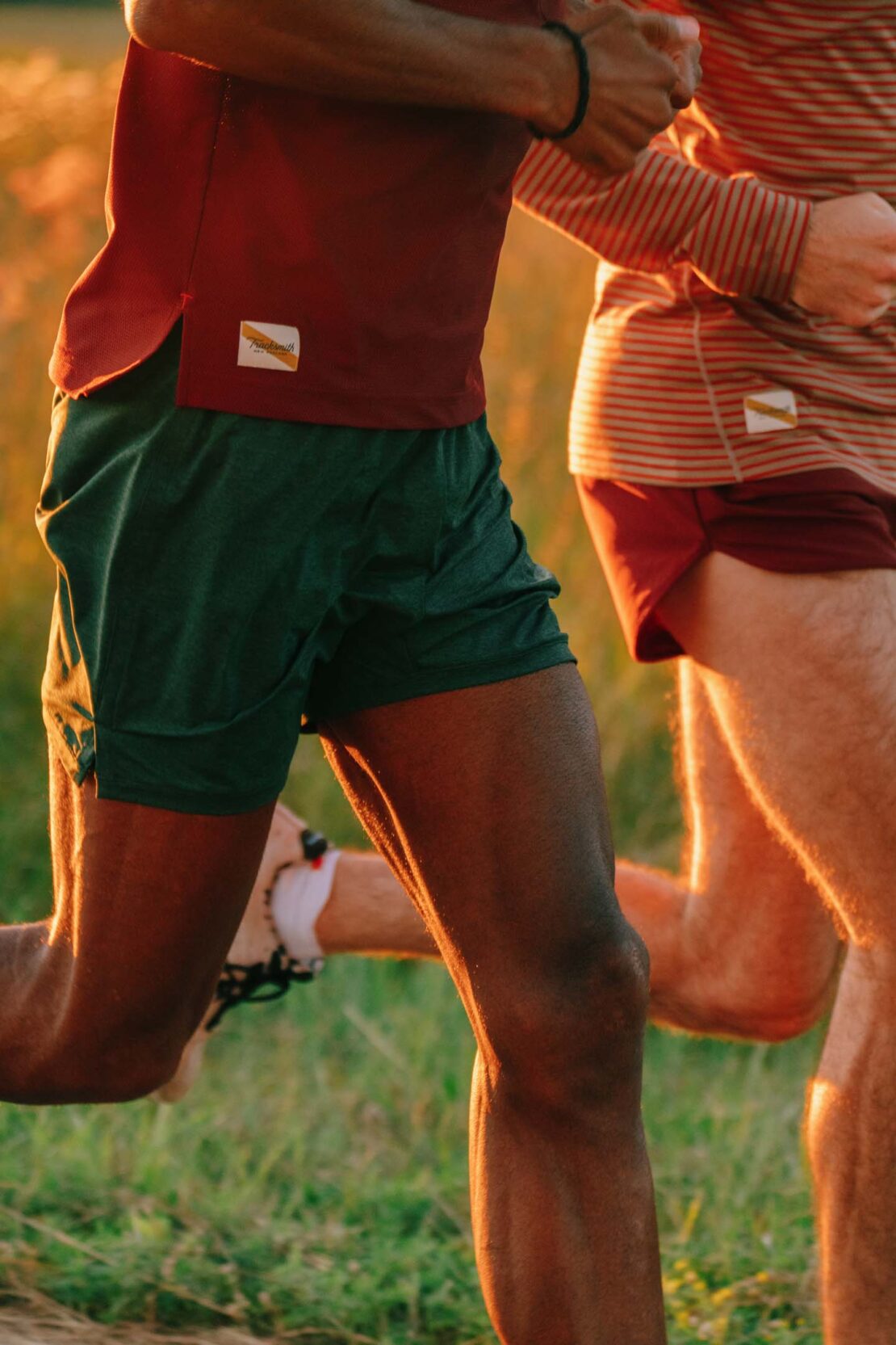 Two runners in athletic apparel jogging through a grassy field during golden hour sunlight.