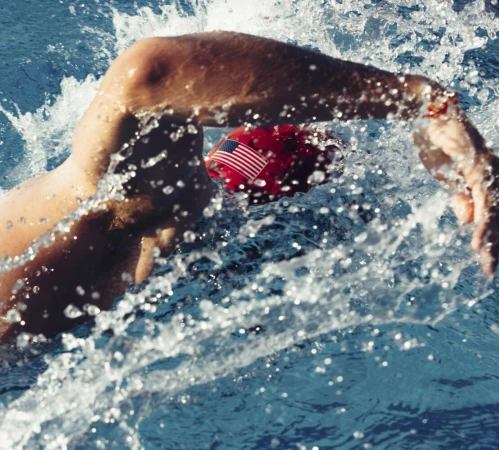 Athlete swimming freestyle stroke in pool with American flag swim cap and splashing water during outdoor training.