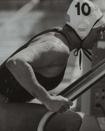 Black and white portrait of a female water polo player wearing cap number 10, gripping the edge of a pool.