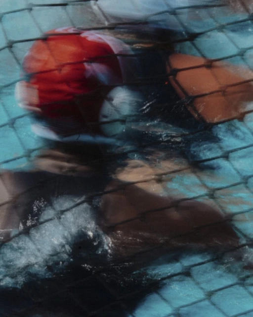 Abstract photo of a swimming pool with a partially submerged multicolored ball and pool tiles visible through the water's surface.