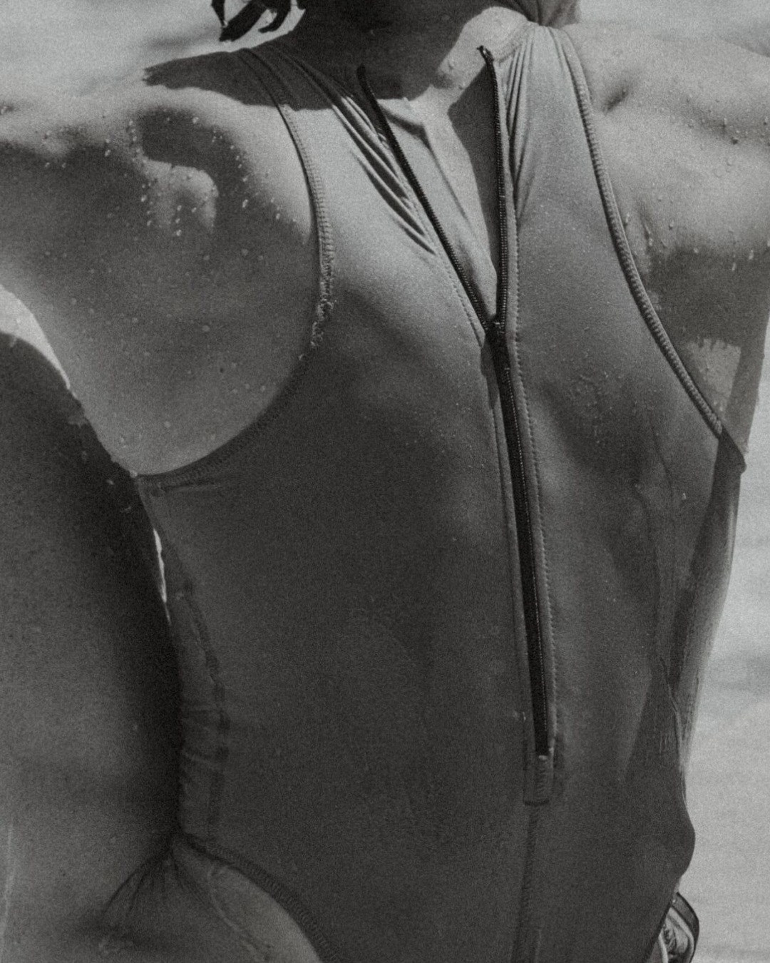 Close-up back view of a person wearing a zipped athletic swimsuit, photographed in monochrome.