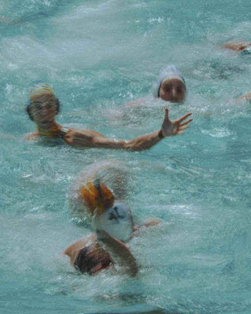 Several water polo players are in action in an outdoor swimming pool, with the focus on their heads and arms in the pool's clear water.