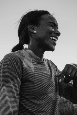 Black and white portrait of a smiling Black woman wearing a striped long sleeve shirt against an outdoor sky background.