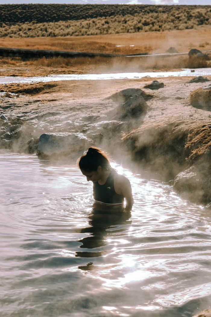 Woman in dark activewear standing in a steaming natural thermal pool in a rugged landscape