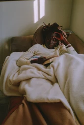 Black woman with dreadlocks relaxing on a sofa under a cream blanket reading a book