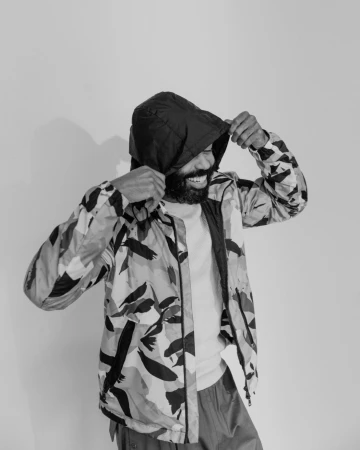 Adult male in patterned jacket pulls up the hood. The jacket has black and white abstract patterns. The backdrop is a plain white background.