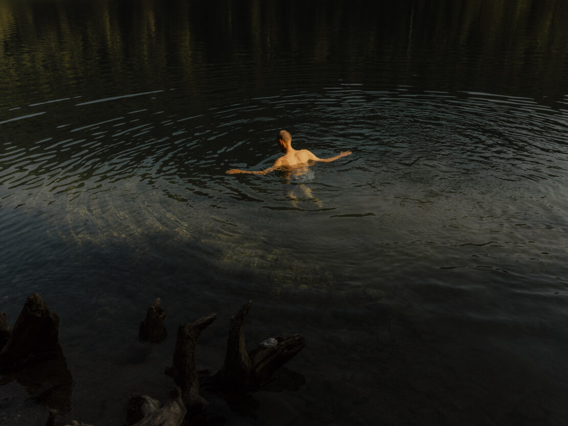Man swimming in a dark mountain lake creating ripples in the water, captured from above by Grant Harder